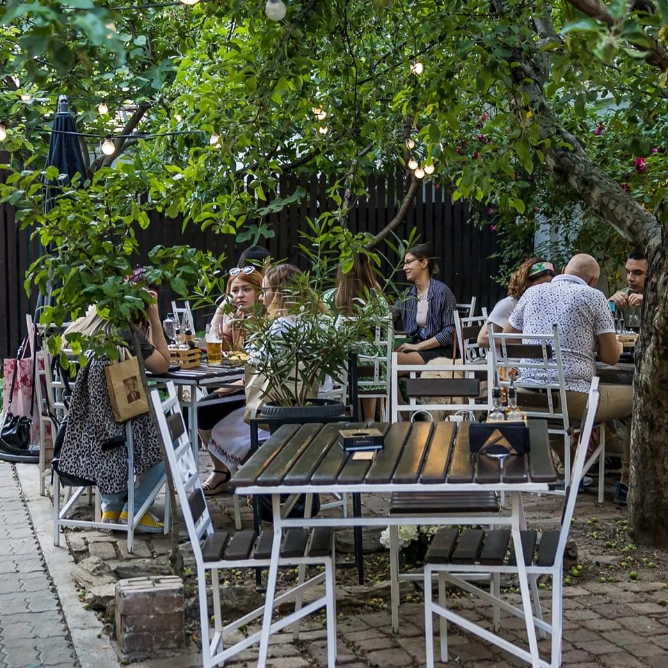 gradina de la Suento, cu mese asezate printre copaci si oemani care iau amsa relaxat