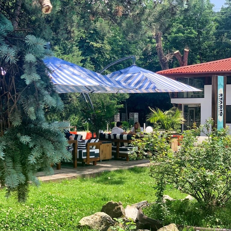 oamni care iau masa sub umbrele de soare, la adapostul copacilor, la restaurant Stadio Park