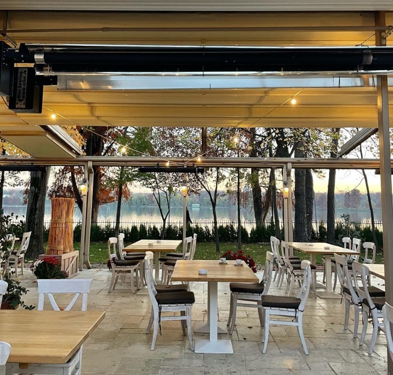 cateva mese și scaune albe sunt asezate pe terasa ancora din herastrau, iar in fundal se vede lacul și padurea