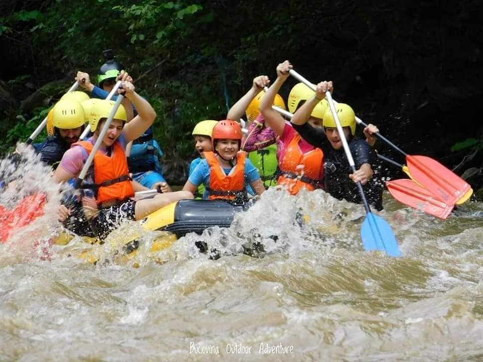 mai multi oameni dau la vasle intr-o barca gomflabila de rafting in apele involburate ale unui rau. Destinații de vară pentru familiile cu copii