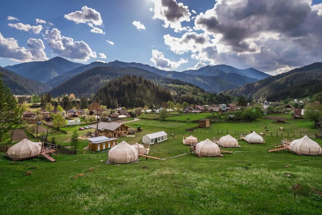 o poiana cu mai multe corturi pentru glamping, iar in spatele lor se vede un munte impădurit