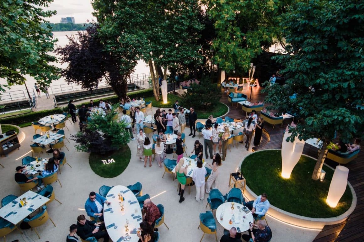 mai multe mese albe sunt asezate pe terasa plina de verdeata a restaurantului tuya. Terase din Herăstrău 