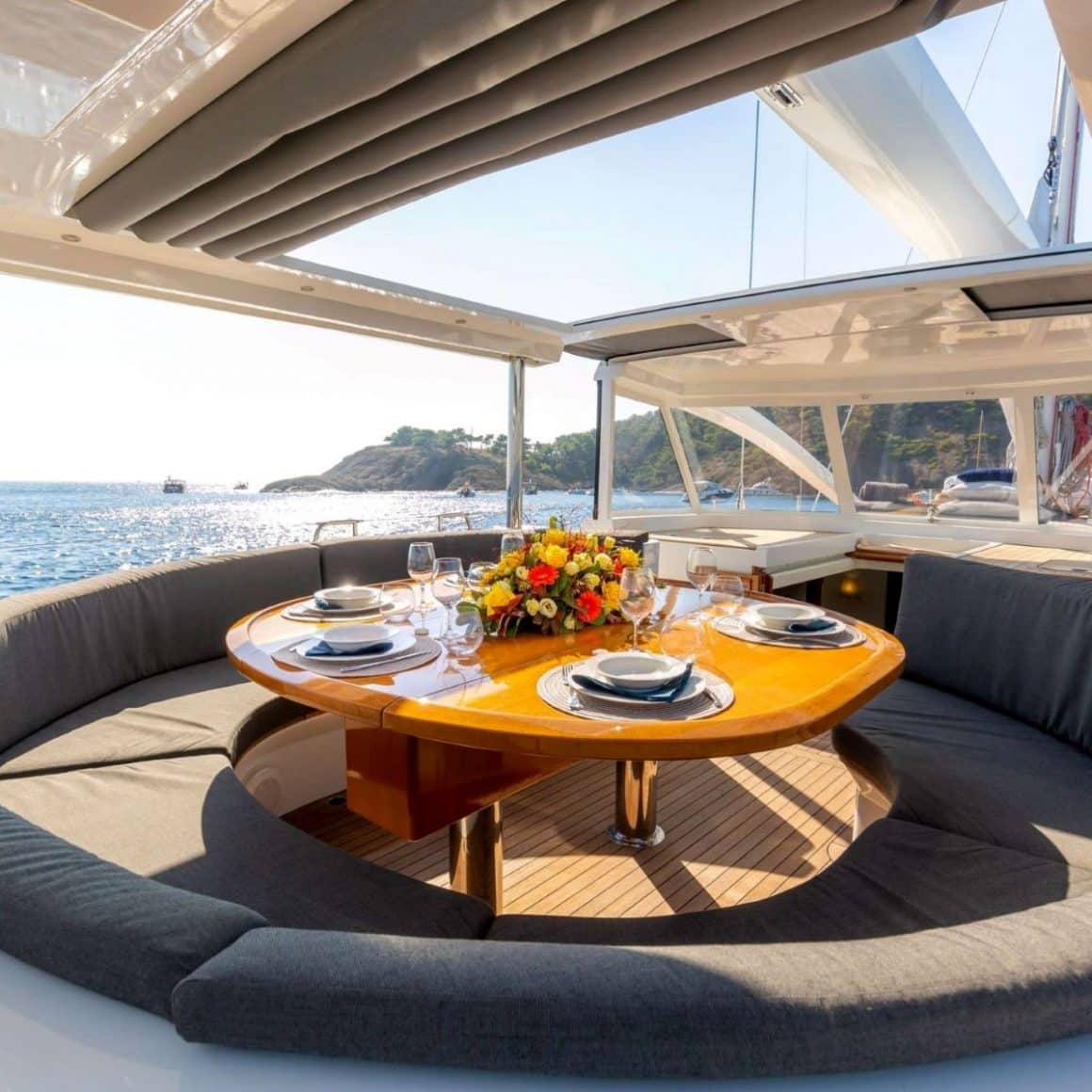 o masa rotunda imprejmuita de canapele confortabile gri, pe un iachtcu trapa deschisa