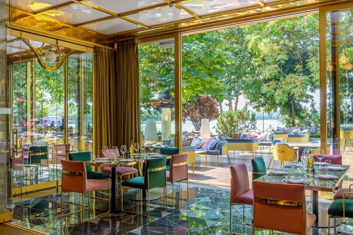 mai multe scaune colorate sunt dispuse in jurul meselor de pe terasa acoperita a restaurantului tuya. Terase din Herăstrău