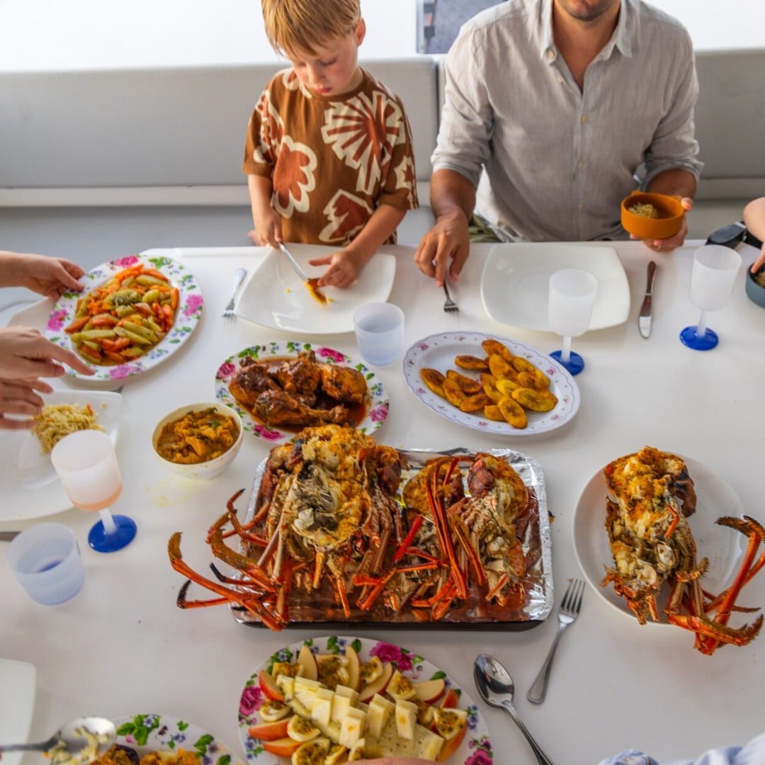 un platou cu fructe de mare este asezat pe o masă alba, iar un tată cu copilul lui se pregatesc sa manace pe punteaiahtului in vacanta