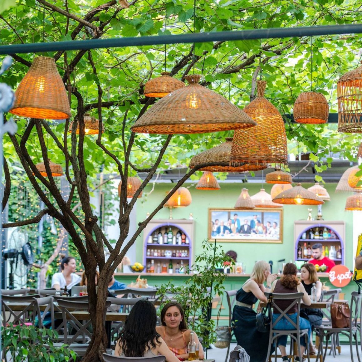 Terasa Gspot Sufrageria din Bucuresti, amenajata in stil retro, cu lampadare atarnate de bolta de vita de vie aflata deasupra meselor. Grădini din București