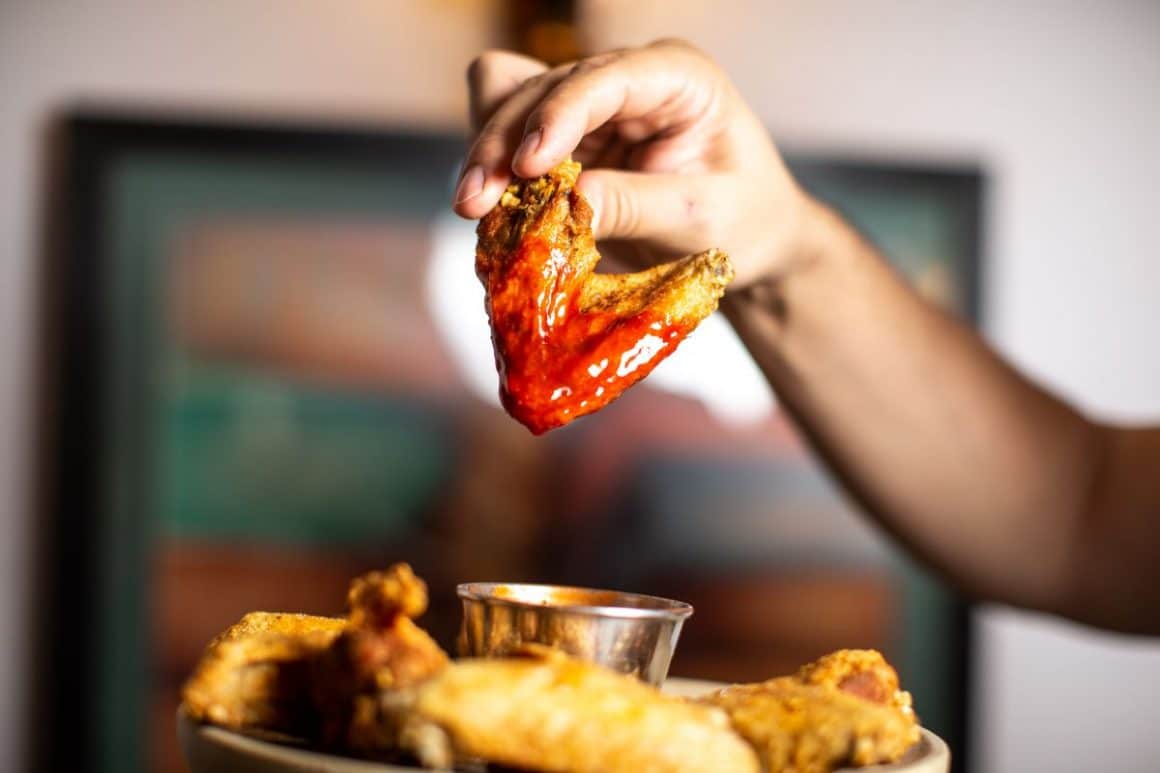 un bărbat scufundă o aripioară în sos picant deasupra unei farfurii cu mai multe aripioare