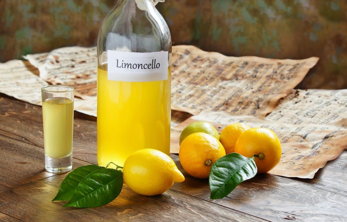 Sticlă de Limoncello, bautura alcoolica italiana, alaturi de cateva lamai si un pahar mic, de shot.