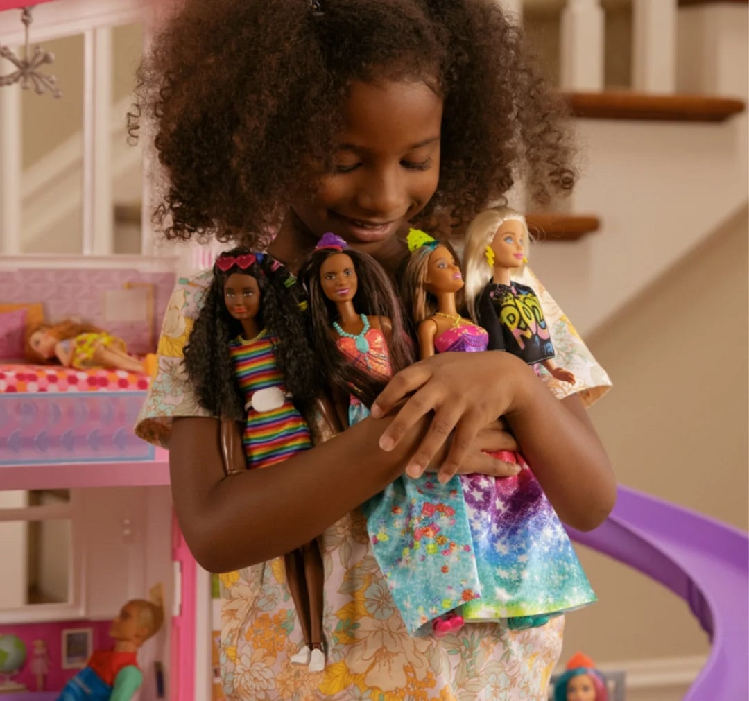O fetita de culoare strange in brate 4 papusi Barbie