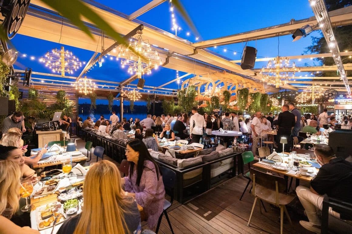 mai multi oameni care iau masa seara, pe terasa Biutiful. Terase din Herăstrău