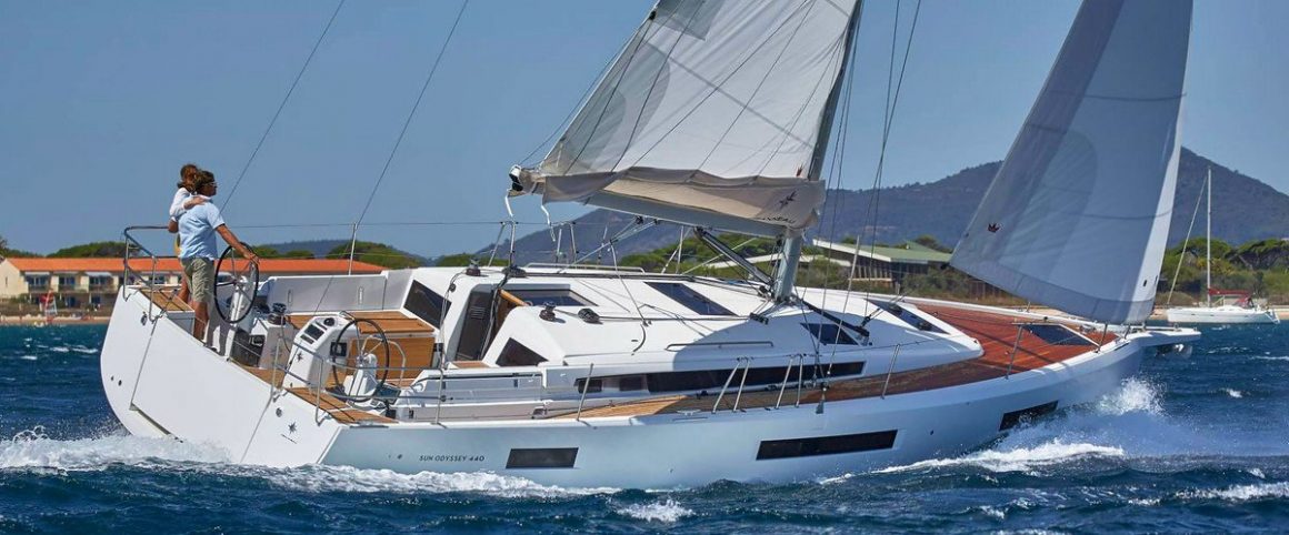 un velier cu panzele ridicate este inclinat de vant și izbeste valurile, iar in spate se vede coasta