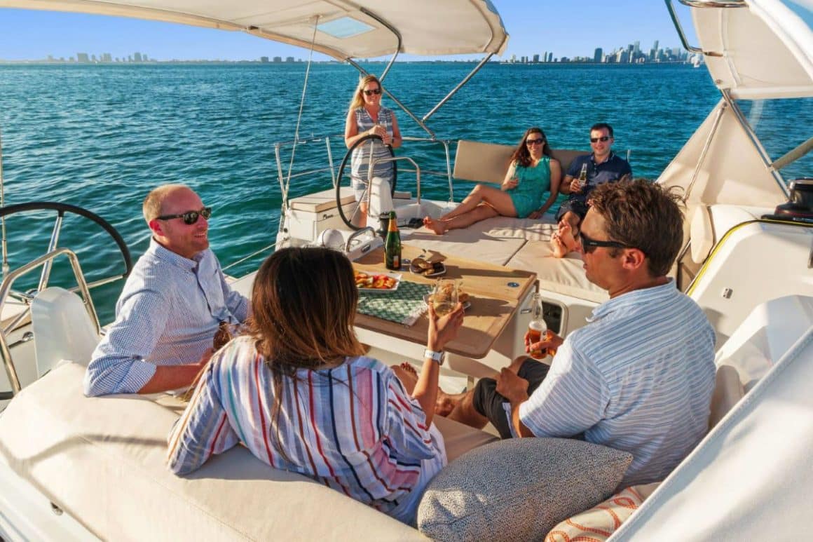 mai multi tineri imbracati in alb se relaxeaza in vacanta pe puntea unui catamaran