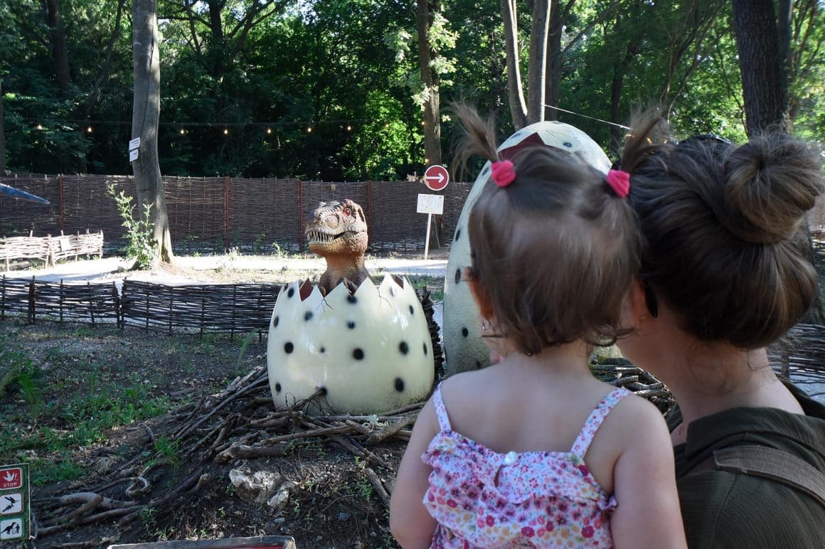 doi copii privesc catre o macheta de pui de dinozaur care eclozeaza în padure