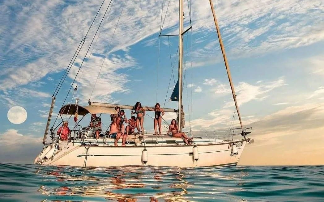 mai multi tineri in costume de baie sunt in vacanta pe un velier cu panzele stranse