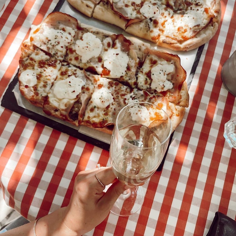 2 platouri cu Pizza si close up cu cineva care tine un pahar de vin in dreptul lor