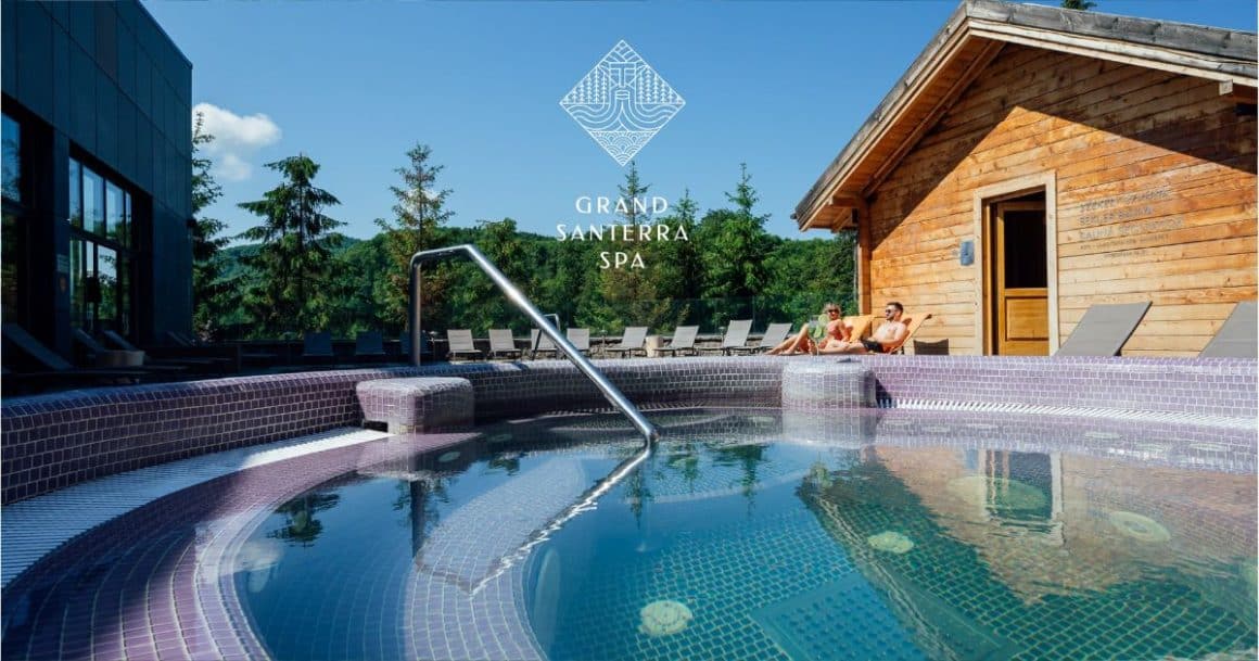 o piscina cu o vila de lemn in spatele ei, iar in plan secund se vede o padure verde