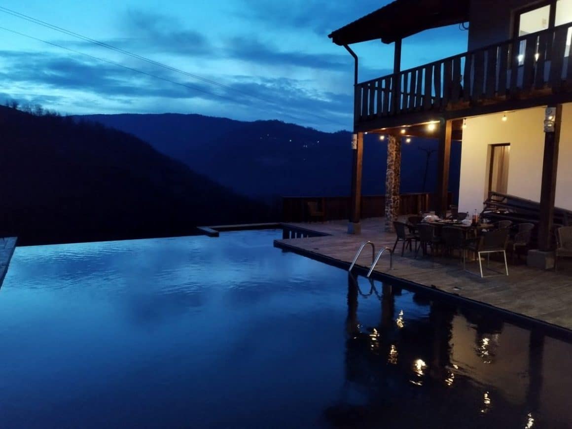 o piscina infinita este fotografiata la apus iar in departare se vad doua dealuri intunecate