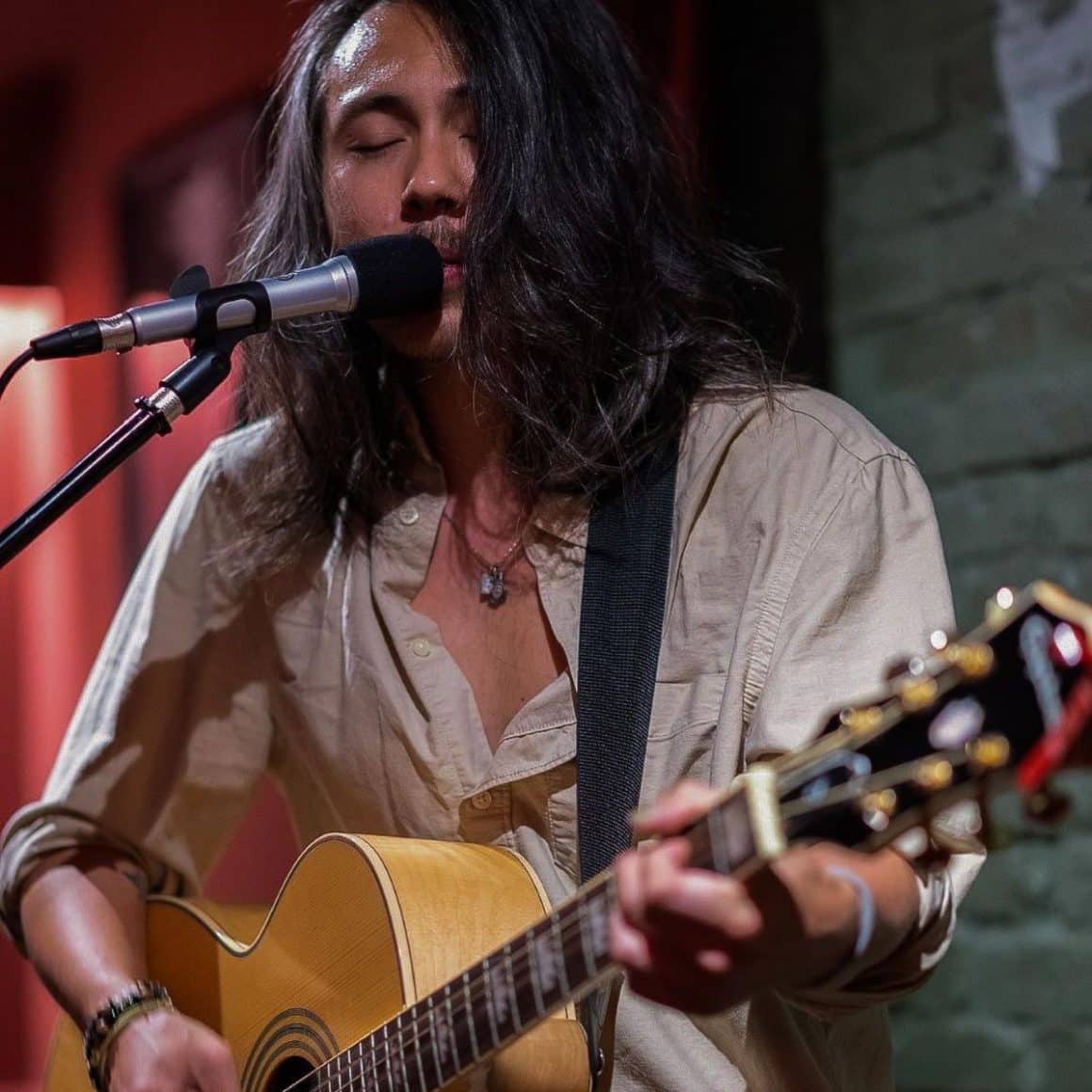 un barbat cu parul lung și camasa canta la chitara