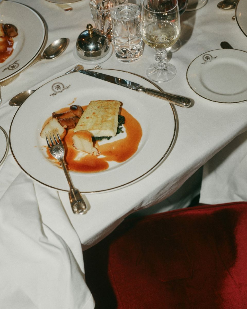 o farfurie cu peste este asezata printre alte pahare si farfurii pe o fata de masa alba