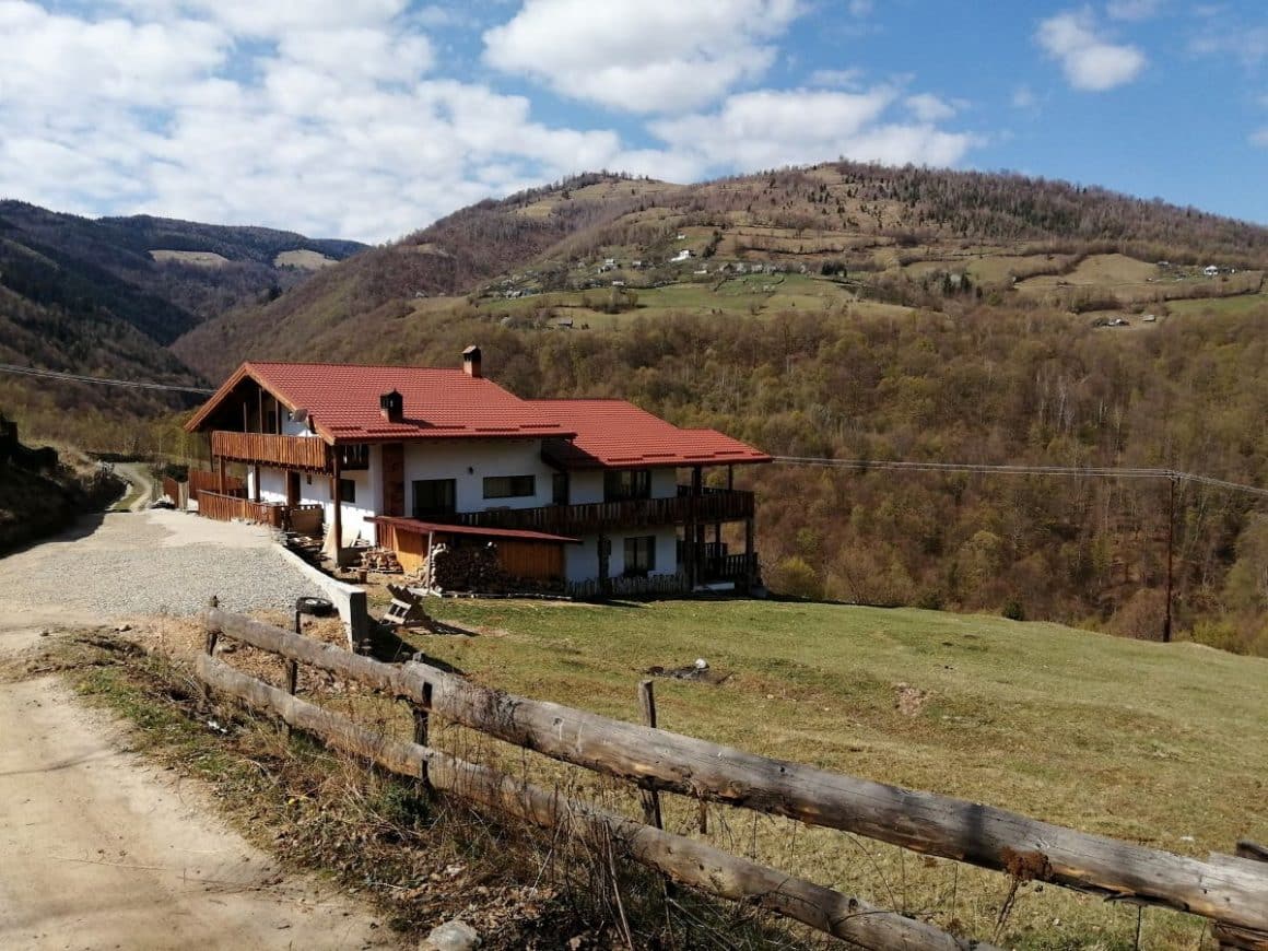 o cabana cu aleea marginita de un gard de lemn, iar in spatele ei este un deal inverzit