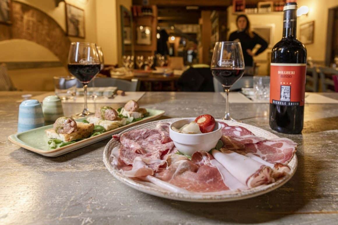 mai multe farfurii cu mancarea traditionala din toscana și cateva pahare si sticle asezate pe o masa 