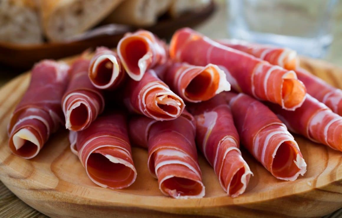mai multe felii de jamon iberico sunt rulate in forma unei tigarete si asezate pe un tocător de bucatarie circular