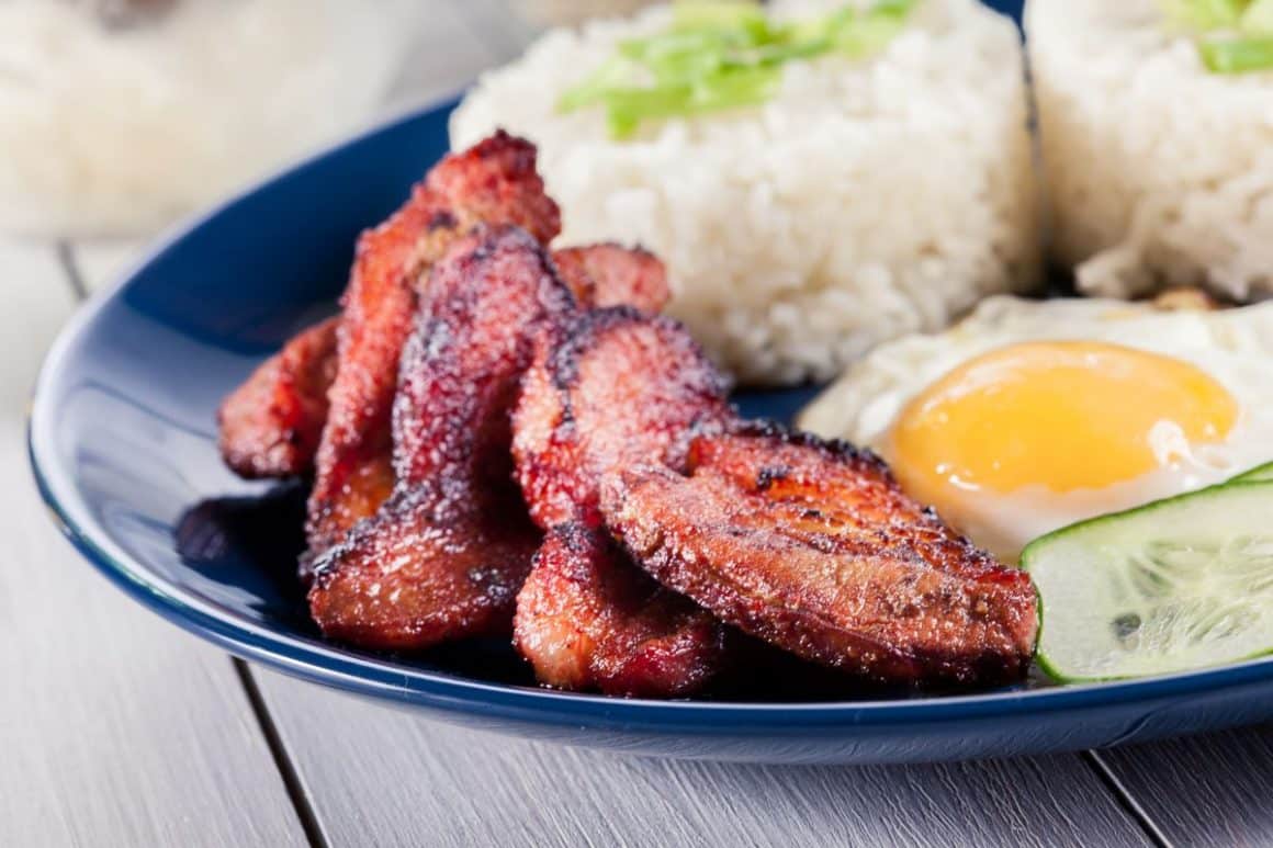 o portie de Arroz A La Cubana – adică orez în stil cubanez cu un ou ochi, o felie de castravete și cateva felii de carne prajita sunt asezate intr-o farfurie albastra