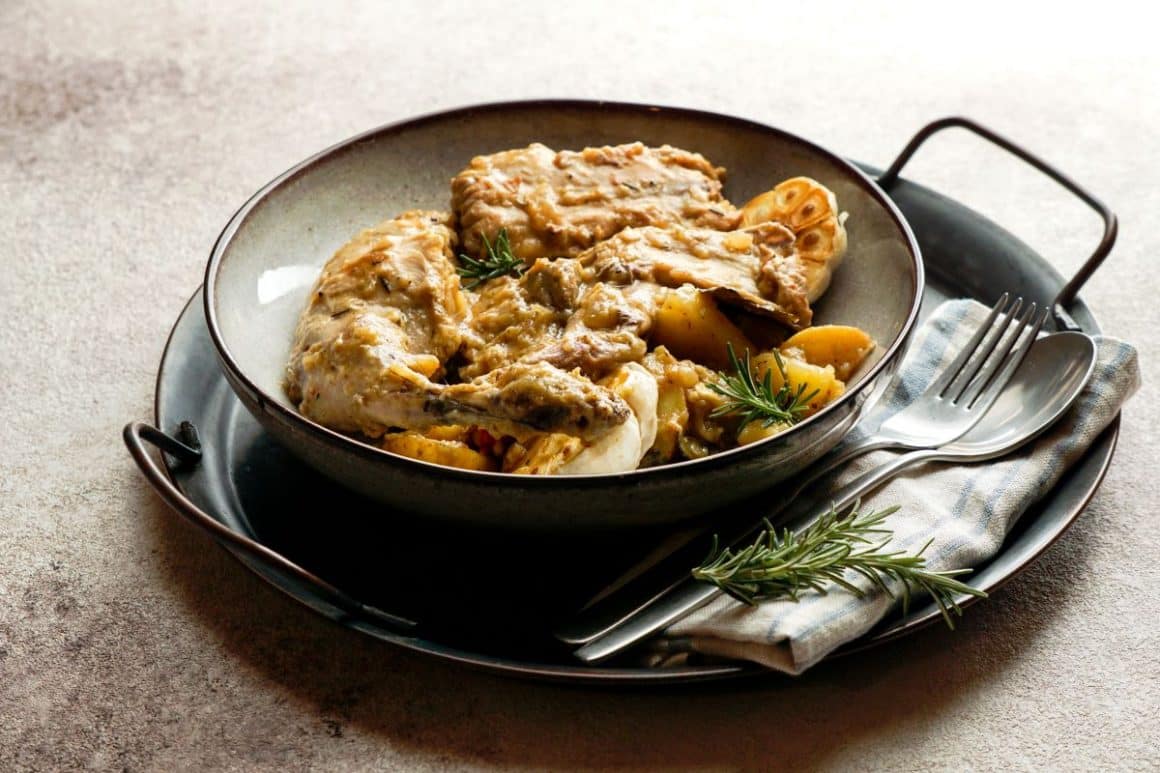 Conejo al salmorejo – iepure în sos sunt asezazateintr-o tava metalica cu manere  alaturi de un servet și tacamuri pe o masa. Mâncare din Tenerife