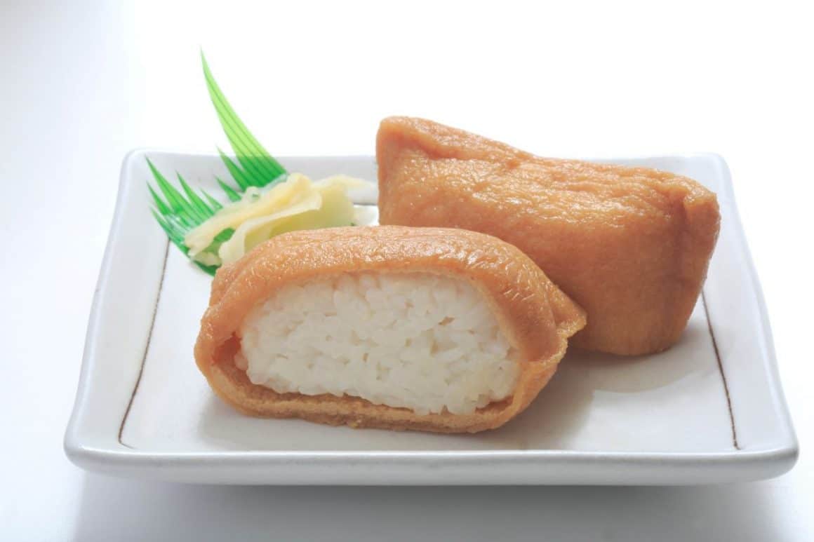 o portie de inari sushi taiata la mijloc, pusa pe o farfurie patrata alba