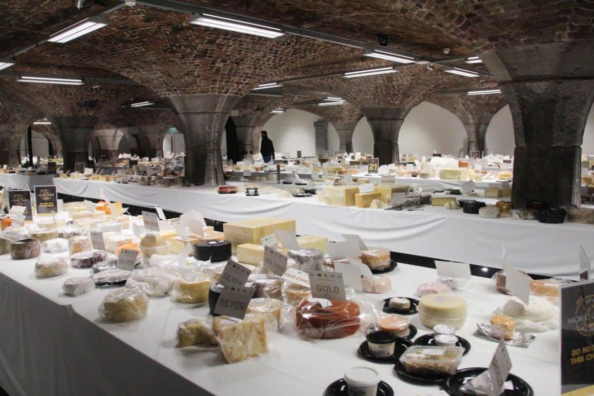 mai multe feluri de branza sunt asezate pe mai multe mese albe, intr-un subsol de clădire cu bolte de caramida. Mâncare din Tenerife