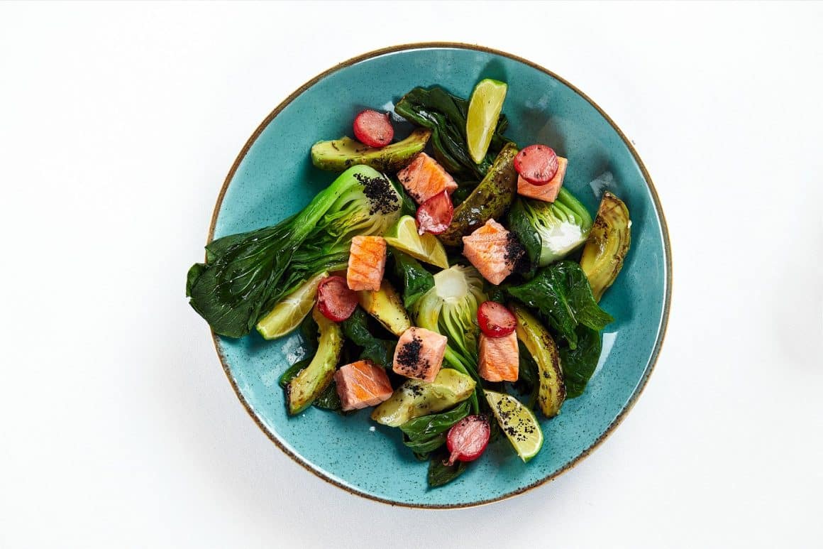 Salmon with artichokes, avocado, close-up, served by the chef with baked salmon and avocado with artichokes in lemon sauce, light background, copy space, top view.