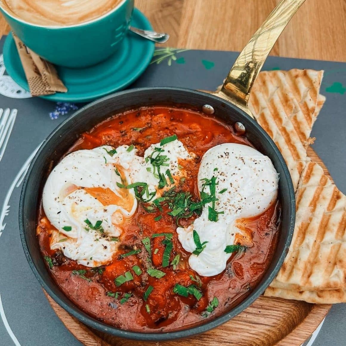 Skakshuka de la B4 Market, in tigaie, servita alaturi de toast, pe un tocator de lemn. Unde mâncăm shakshuka în București