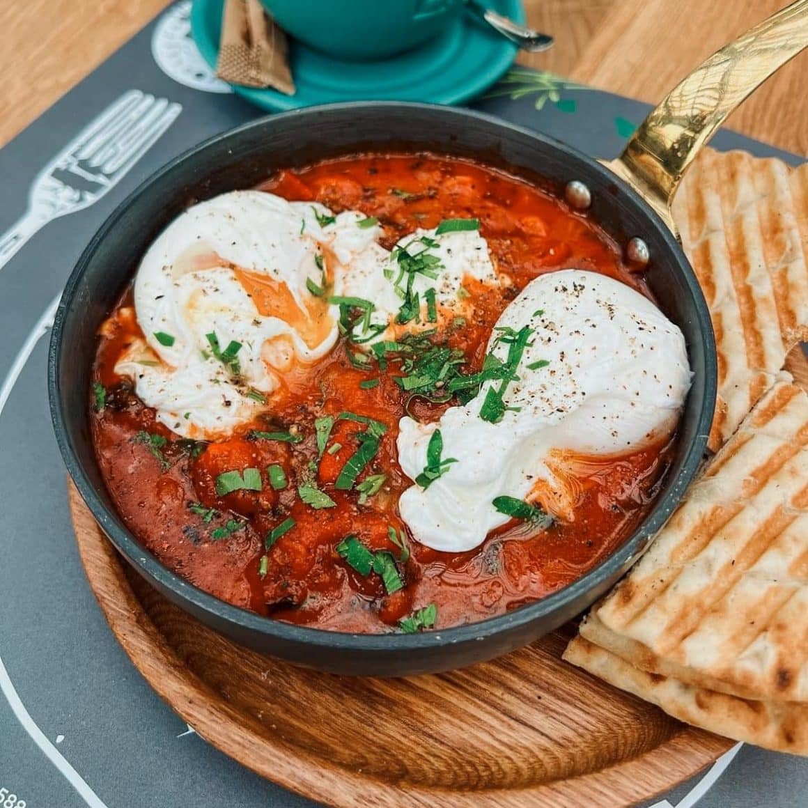 Skakshuka de la B4 Market, in tigaie, servita alaturi de toast, pe un tocator de lemn