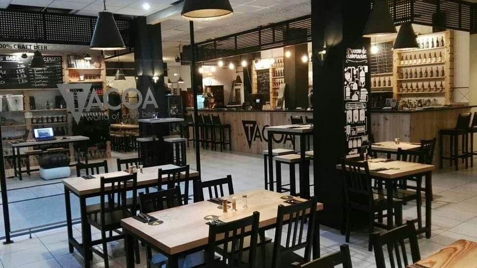 Interiorul restaurantului Tacoa din Tenerife, cu mese si scaune de lemn și barul localului in fundal