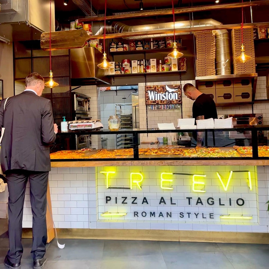 un barbat in costum isi comanda pizza la felie din restaurant