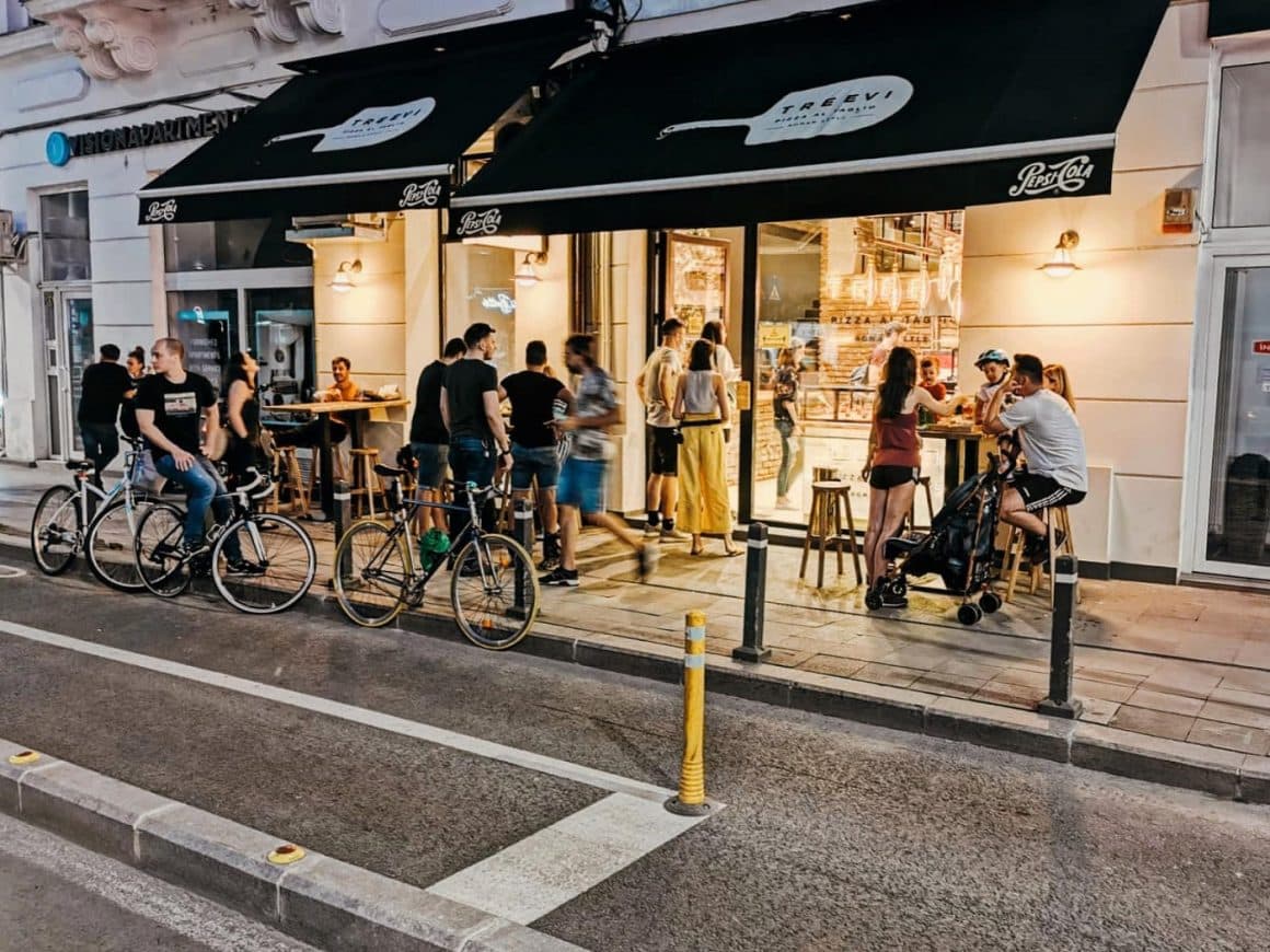mai multi tineri la mese intinse afara, pe strada, in fata restaurantului Treevi Pizza Al Taglio din București