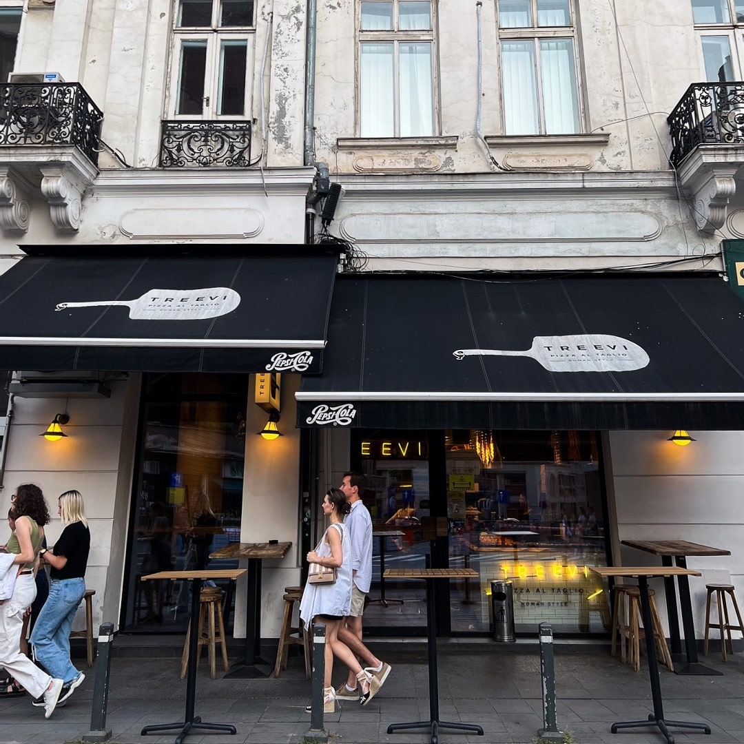 oameni care trec pe strada prin fata pizzeriei treevi