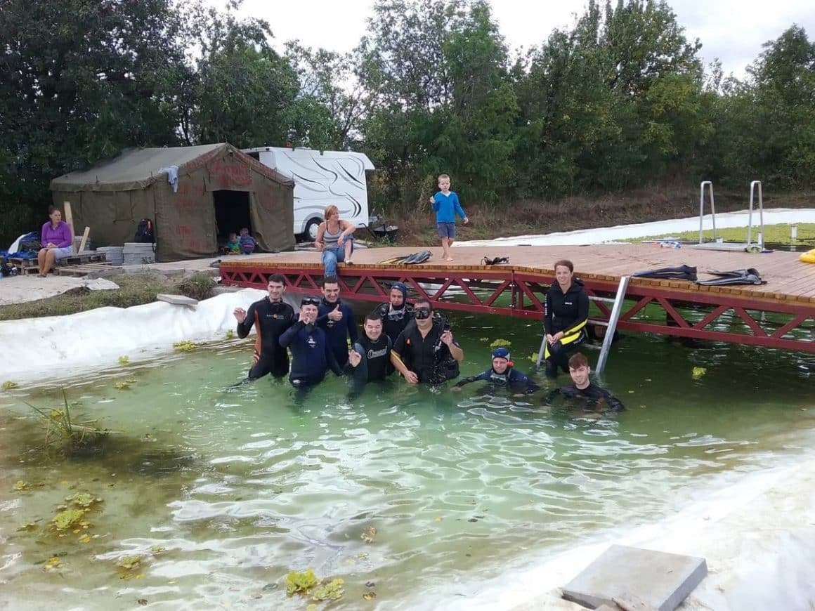 mai mulți tuiști sunt inbracati in costume de scafandru, într-un râu, lângă un pod.