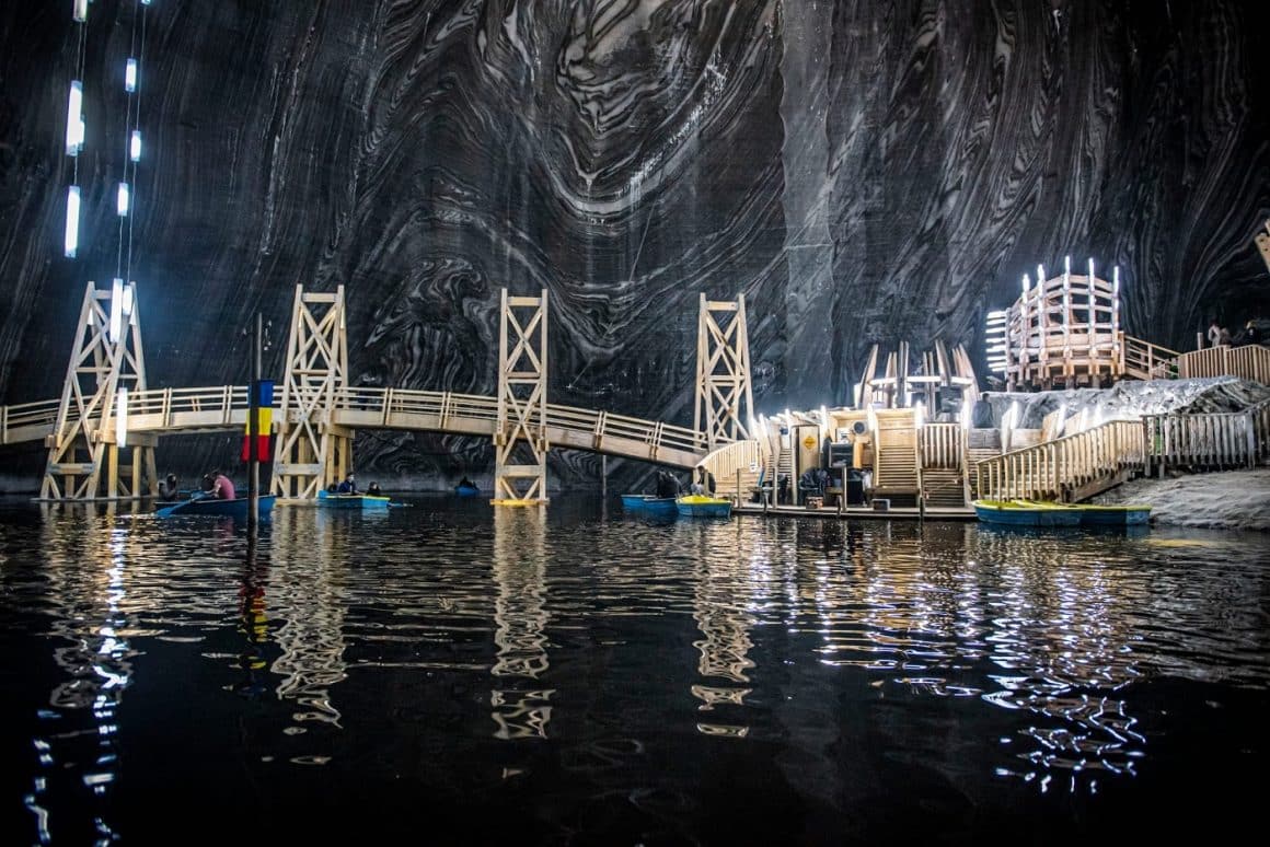interiorul uneia dintre salinele din România cu un lac subteran, lumini și un podeț de lemn sub peretii de sare. Salina Turda