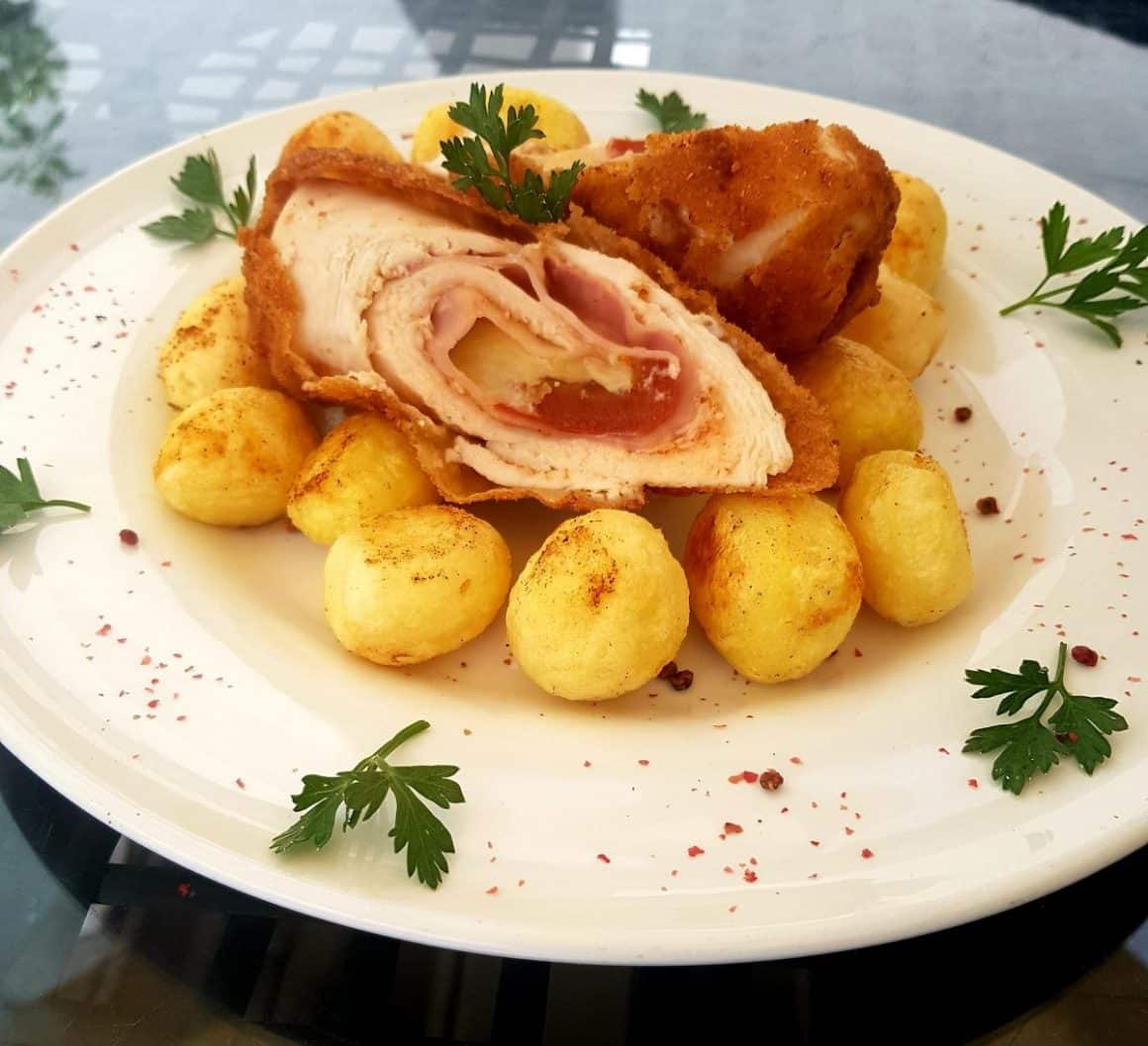 un rulou de carne este asezat peste mai multi cartofi mici și intregi, pe o farfurie rotundă decorată cu frunze de pătrunjel