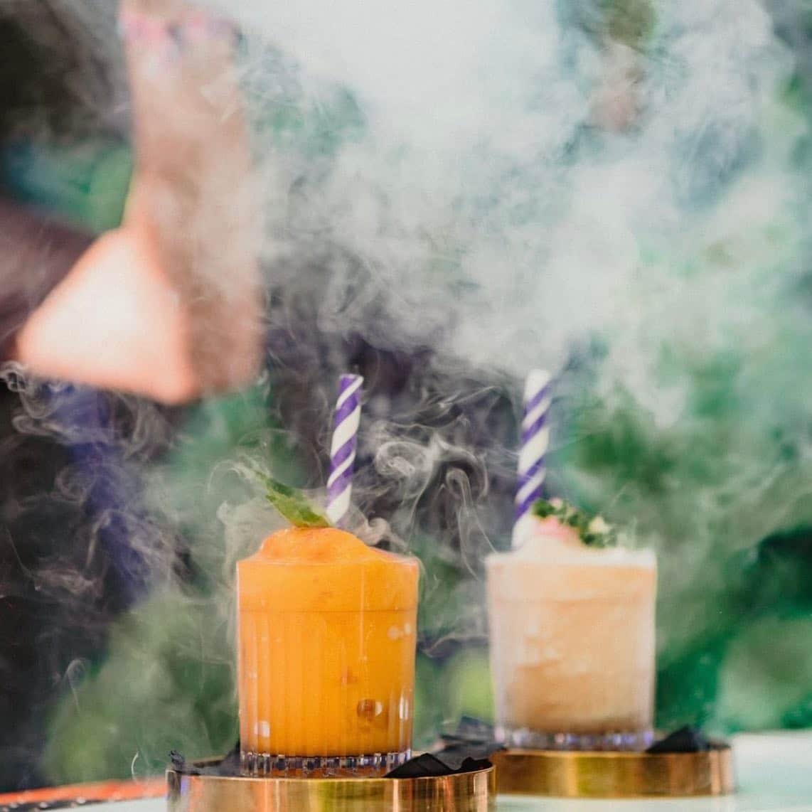 doua pahare de cocktail colorate sunt invaluite in fum și au doua paie groase