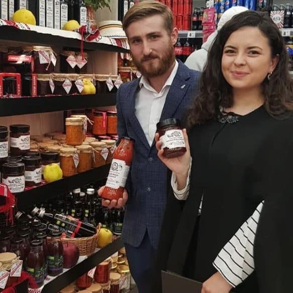 doi tineri îmbrăcați elegant pozează în fața unui raft de magazin cu produse locale