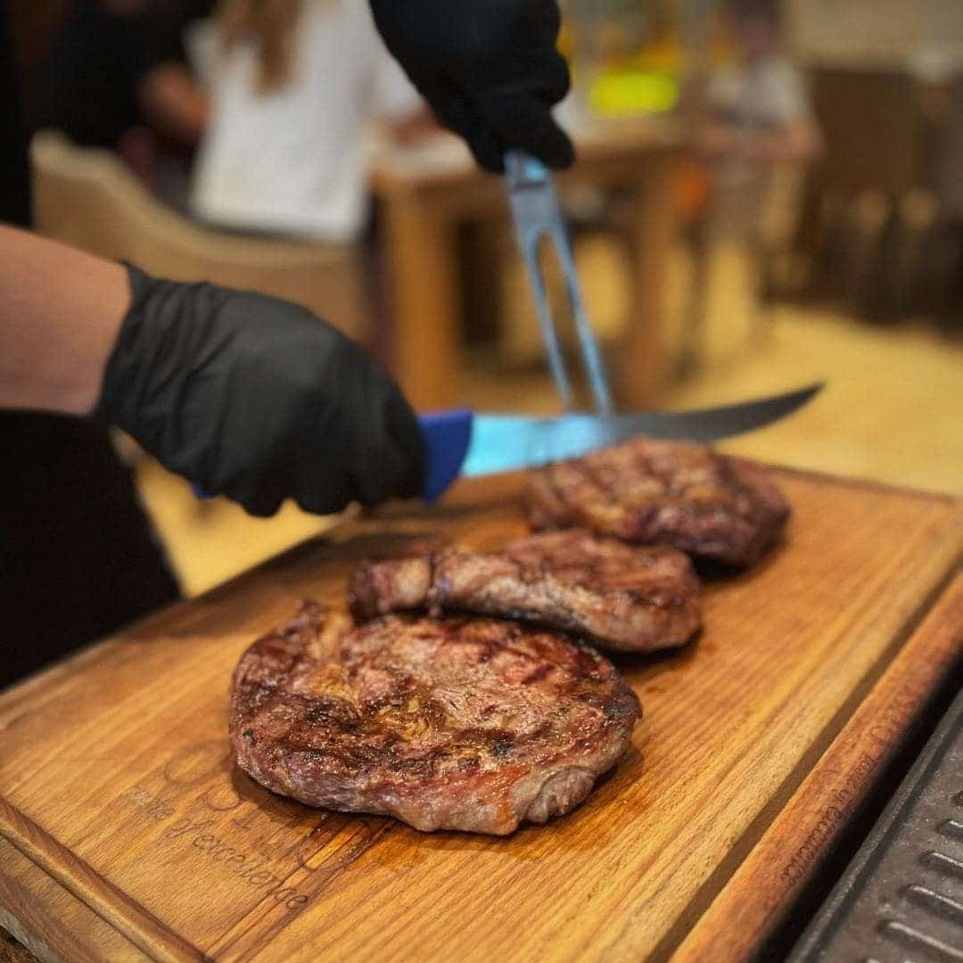 bucatar taie 3 felii de steak pe un tocator de lemn