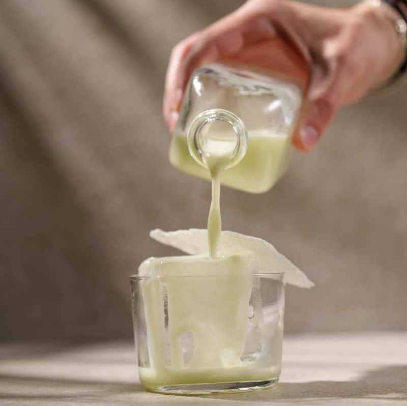 o mana de femeie toarna un cocktail in pahar dintr-o sticlă mică și pătrată