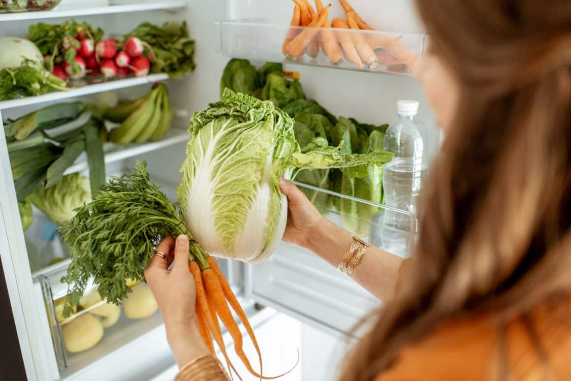 Woman taking fresh cabbage and carrot from the refrigerator at home, close-up view