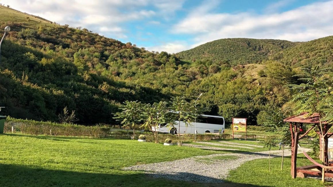 intr-un peisaj montan stă parcată o rulotă, printre copaci și verdeață