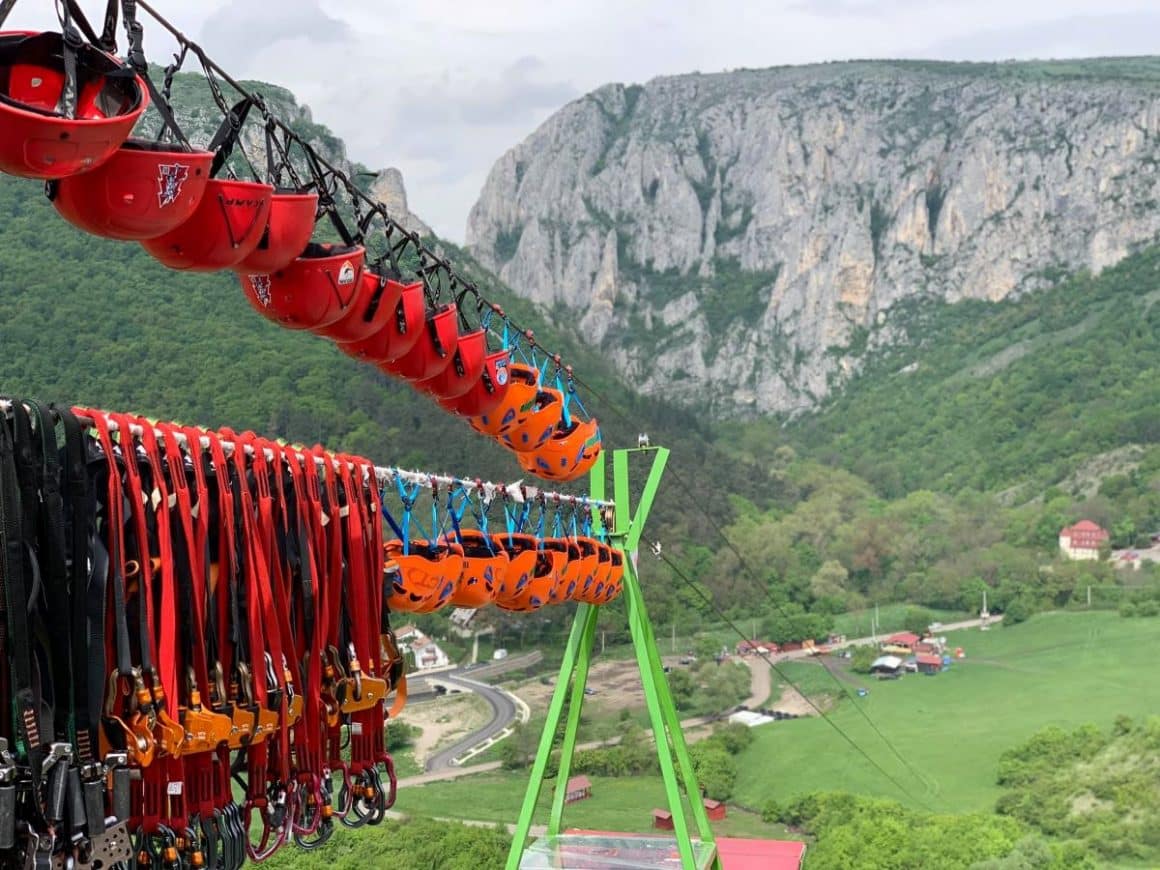 mai multe echipamente pentru tiroliana sunt asezate unul lângă altul, iar în spate se vede un peisaj montan