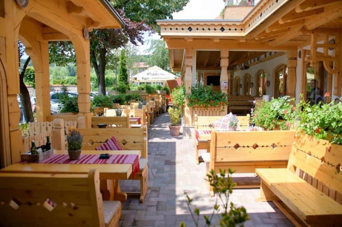 terasa unui restaurant rustic cu mese de lemn masiv și arbuști decorativi