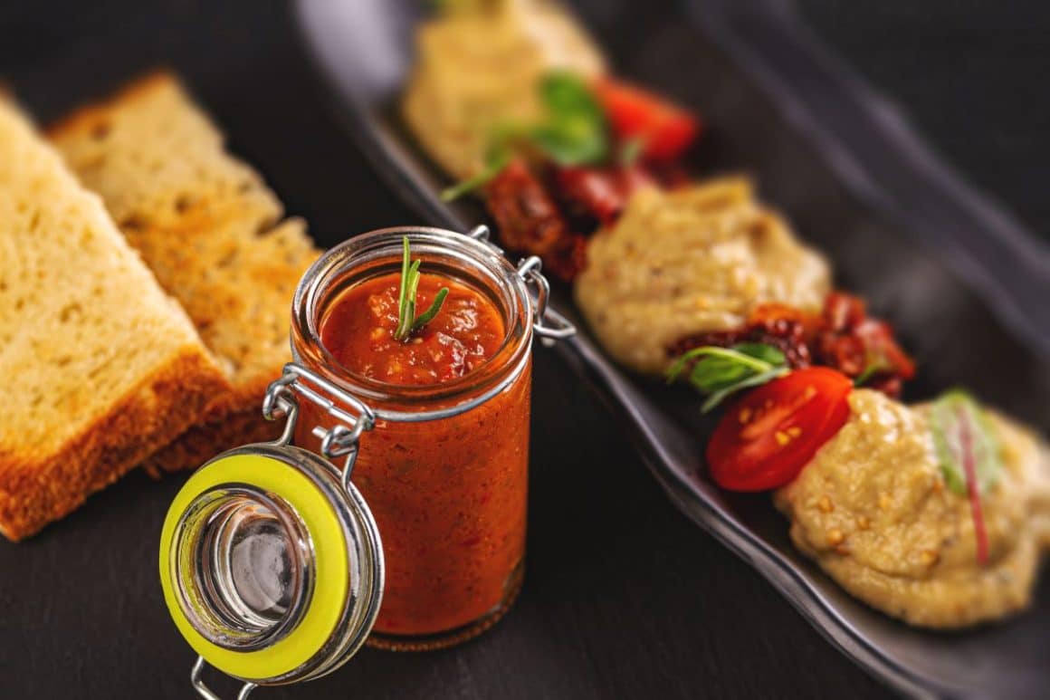 un borcan de zacusca de la producători locali este asezata langa două felii de pâine și un platou de salata de vinete