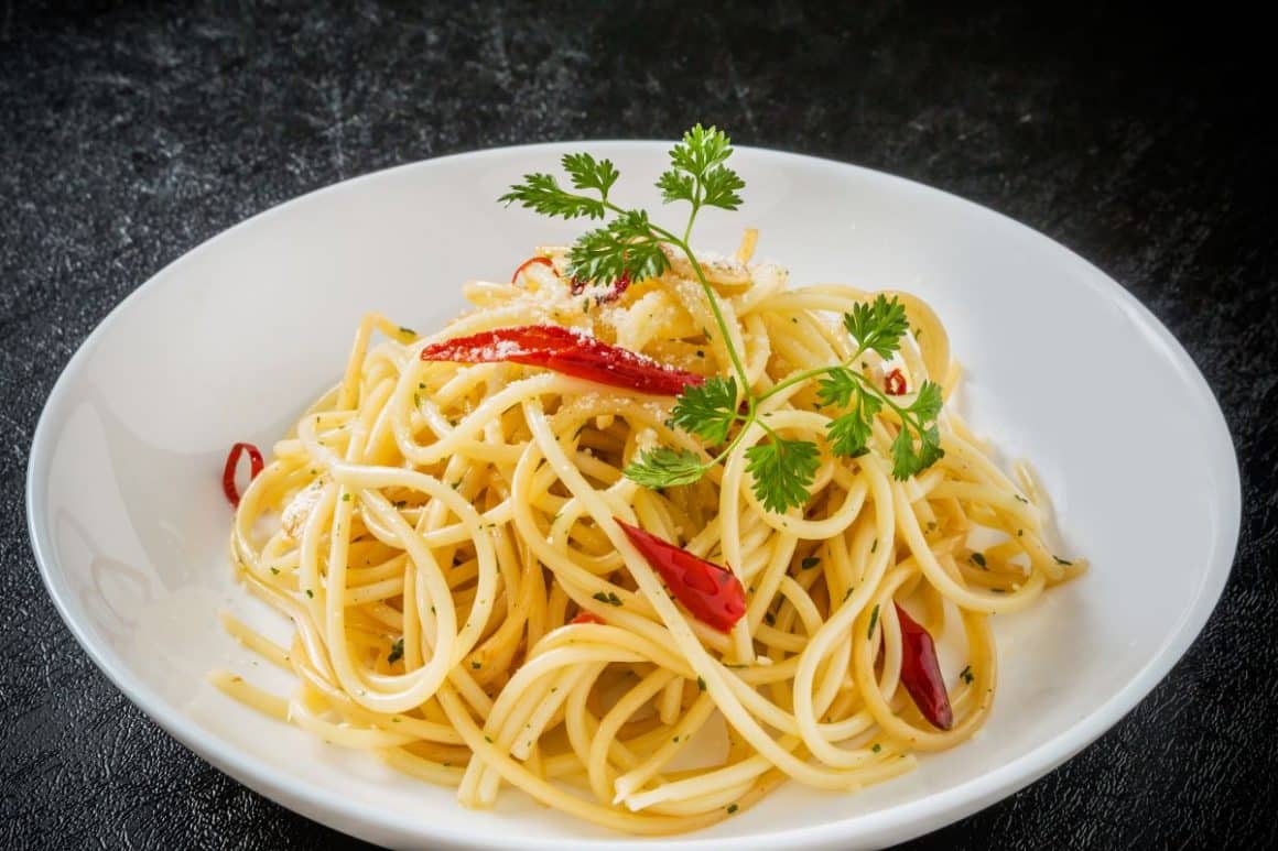 o portie de paste cu sos Aglio e Olio, servite intr-o farfurie alba, cu ardei iute roșu și o crenguță de coriandru verde